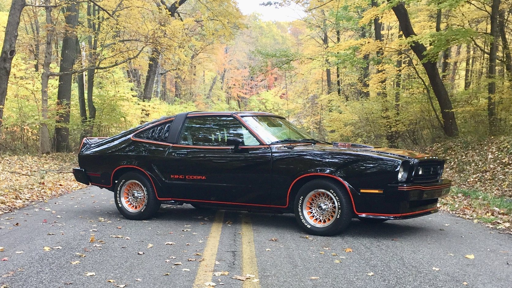 Black 1978 Ford Mustang II King Cobra with gold pinstripes on an autumn road