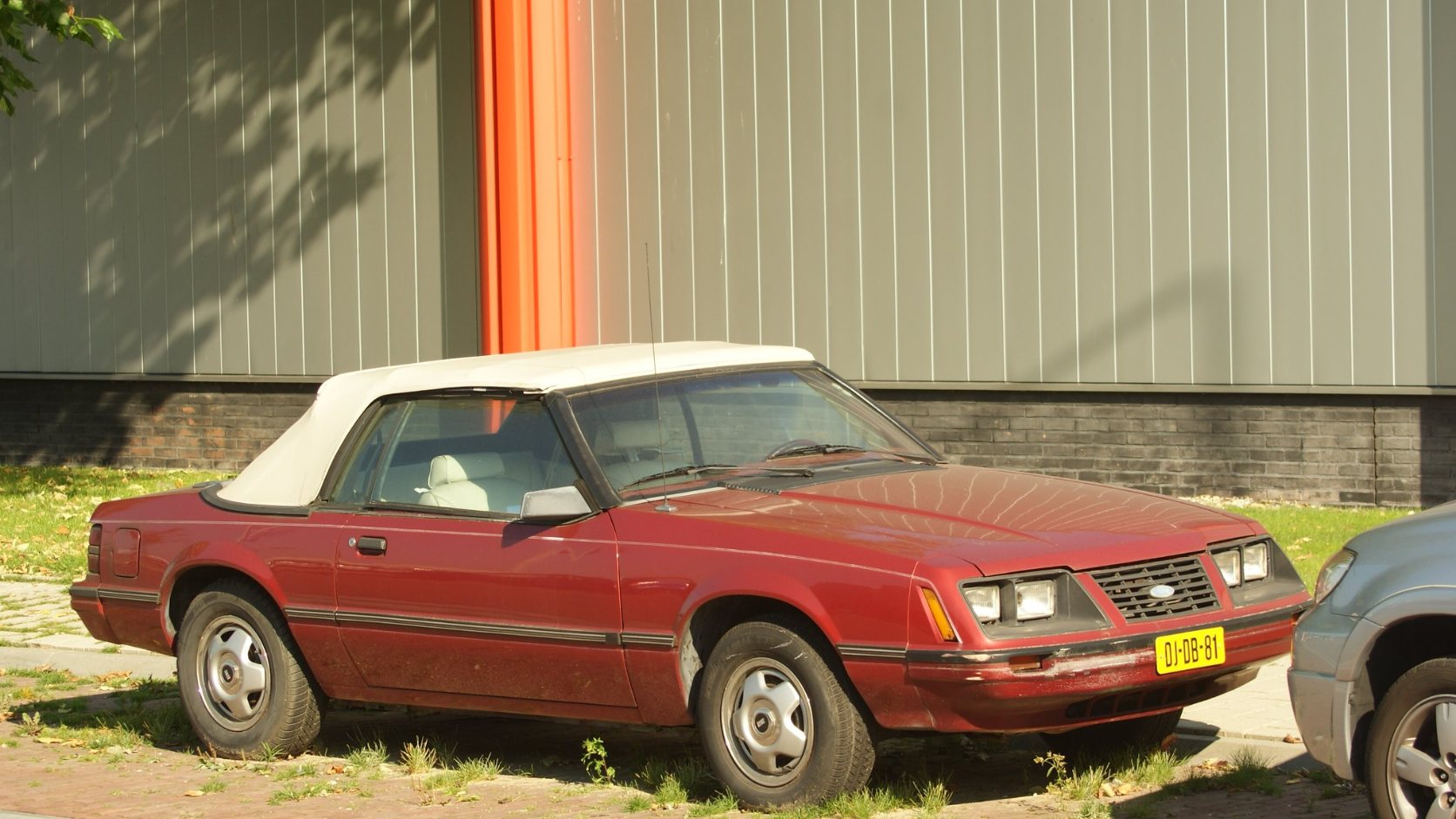 Red 1983 Ford Mustang convertible with a white top, front three-quarter view